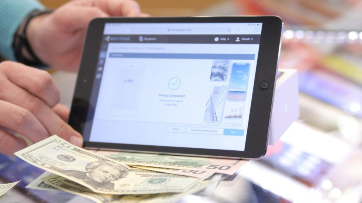 A person holding a tablet that shows a completed online money transfer, with banknotes below it