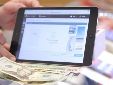 A person holding a tablet that shows a completed online money transfer, with banknotes below it